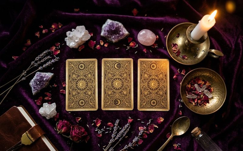Cartas de tarot extendidas sobre tela púrpura y velas para lectura espiritual